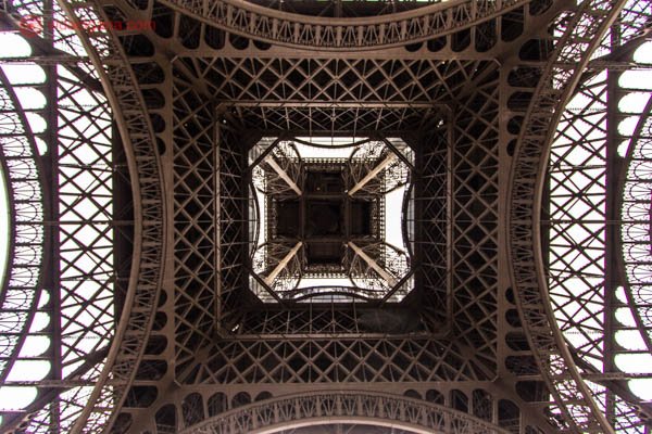 A Torre Eiffel vista de baixo, toda angulosa e feita de aço. Possui uma tonalidade marrom.