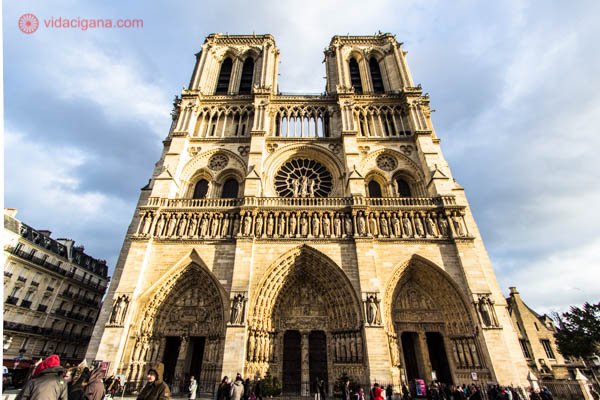A catedral de Notre Dame de Paris, uma das igrejas mais famosas no mundo, que fica em Paris. Foto feita em um dia frio e nublado, mas felizmente fez sol na hora da foto, onde a igreja aparece iluminada por ele, com uma leve tonalidade amarelada. A catedral possui duas torres em sua fachada e estilo gótico.