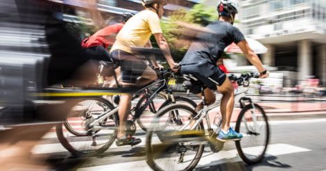 dois homens andando de bicicleta na avenida paulista em são paulo. Os dois estão usando capacetes. A foto é um panning das bicicletas em movimento e tudo ao redor borrado.