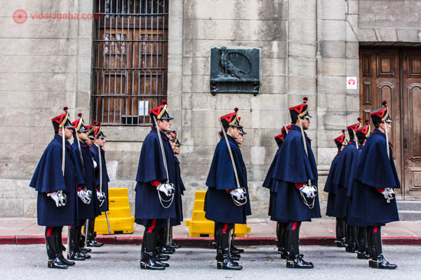 Vários guardas com uniformes exóticos está enfileirados na Plaza Constituición, em Montevidéu, no Uruguai, em frente a um edifício. Todos eles seguram espadas.