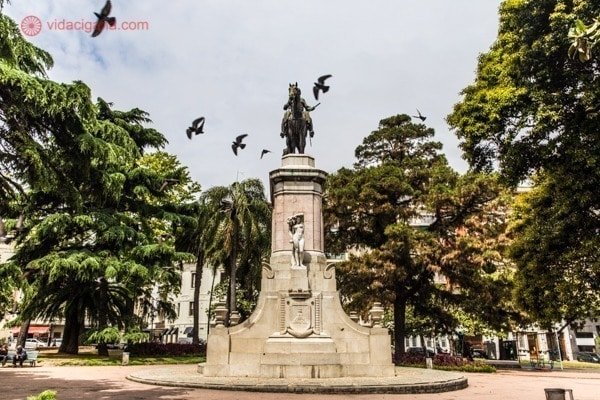 a estátua na praça zabala em montevidei, com um homem em um cavalo e vários pássaros voando ao seu redor.