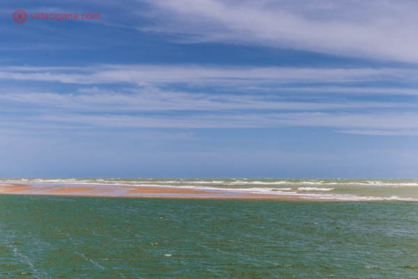 O delta do São Francisco, entre Alagoas e Sergipe, com uma duna de areia dividindo o mar do rio. O céu é azul e a água, verde.