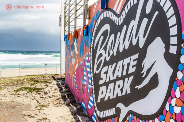 Onde ficar em Sydney: A praia de Bondi, em Sydney, com as ondas batendo ao fundo. Do lado direito, em primeiro plano, está a parede de um skate park toda colorida.