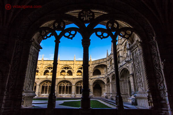 O pátio do Mosteiro dos Jerônimos em Lisboa visto através de uma janela enorme totalmente adornada. O pátio está iluminado com o final do sol e a foto foi tirada durante o pôr do sol. O céu está azul