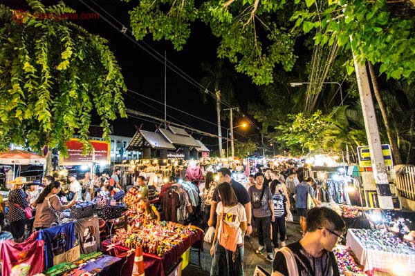 Onde ficar em Chiang Mai: a região do night bazaar em Chiang Mai, na Tailândia, repleto de barraquinhas vendendo todos os tipos de coisas, de roupas a comida, com muitos turistas e locais andando por entre as barracas. Algumas árvores e muita luz.