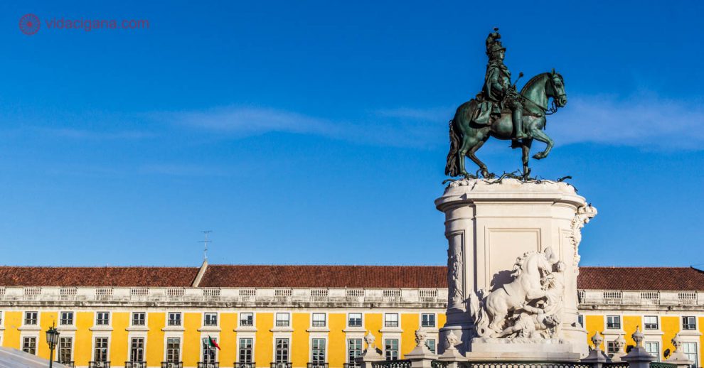 O que visitar em Lisboa: A estátua equestre de D. José I na Praça do Comércio em Lisboa, cercada de prédios amarelos de telhas ocre. O céu no dia desta foto estava incrivelmente azul.