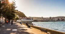 O que fazer em Wellington: A capital da Nova Zelândia é cheia de surpresas, com suas lindas ruas. Na foto vemos Oriental Bay, uma das praias mais frequentadas de Wellington, com pessoas pegando sol na calçada, árvores e restaurantes na beira do mar.