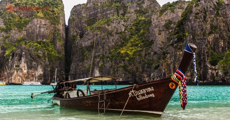 Onde ficar em Koh Phi Phi: Um longtail boat em Maya Bay, em Koh Phi Phi, ancorado na praia de areias claras e águas verdes claras e transparentes. No fundo, os icônicos paredões de Maya Bay, altos e com vegetação entre suas rochas.