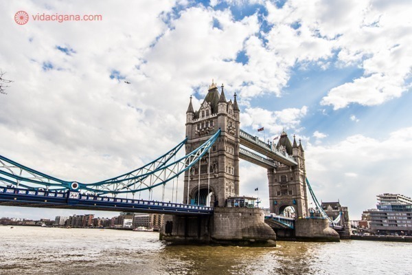 A mais famosa ponte de Londres, a Tower Bridge, vista da Torre de Londres, na beira do Rio Tâmisa, com suas duas torres, cabos azuis e passarela. O céu nesse dia está parcialmente nublado.