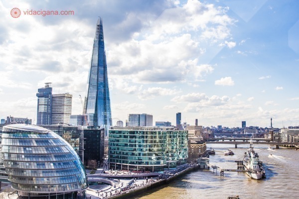 A parte mais moderna de Londres, com prédios como o The Shard e o City Hall vistos do topo da mais famosa ponte de Londres, a Tower Bridge, no Rio Tâmisa. O céu está parcialmente nublado.