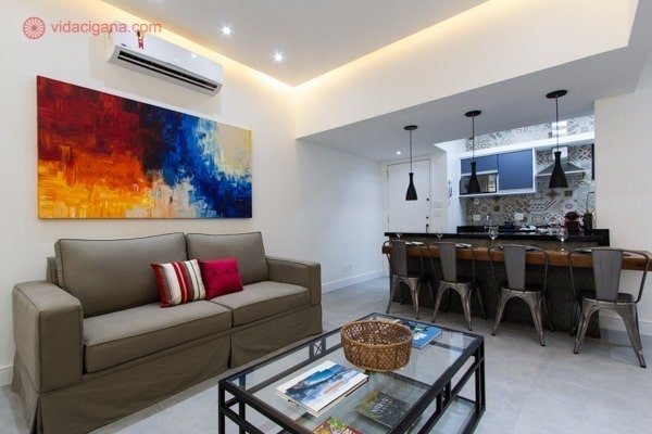 Sala no rio com sofá cinza, quadro bem colorido, cozinha americana com visual moderno