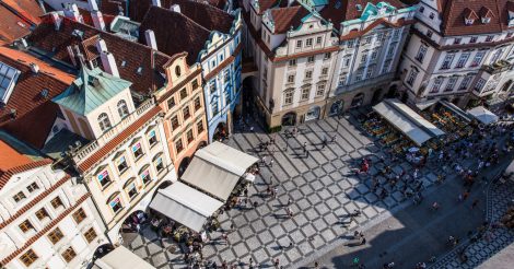 Onde ficar em Praga: A Cidade Velha vista do alto da Torre do Relógio. Chão de piso quadriculado cinza claro e escuro, casinhas antigas de 4 andares de diversas cores, e muitos turistas transitando pela pequena praça que tem em frente