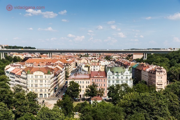 Onde ficar em Praga: O bairro de Vysehrad visto de cima de seu castelo, com suas casinhas coloridas e um enorme viaduto passando por cima delas. O céu está azul
