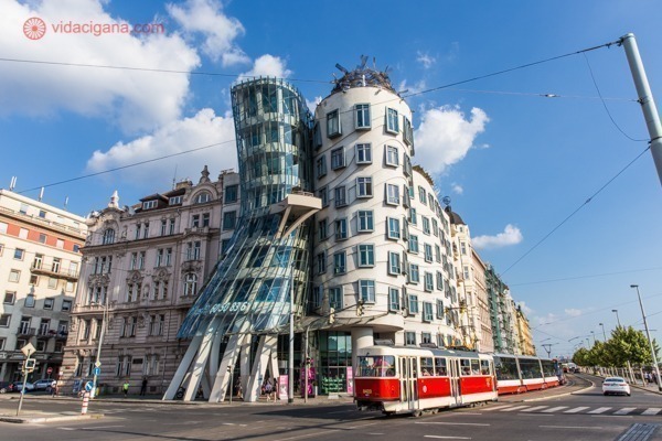 Onde ficar em Praga: A exótica Casa Dançante em Praga, com sua arquitetura louca, retorcida e com vidros transparentes. Um bonde vermelho passa na rua em frente
