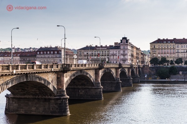 Onde ficar em Praga: Uma ponte cheia de arcos acima da água, com seus prédios baixos e céu azul do entardecer