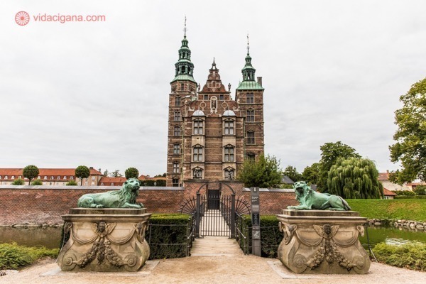 Onde ficar em Copenhague: O castelo de Rosenborg, com suas paredes ocre, torres verdes, com leões protegendo sua entrada. O céu está nublado.