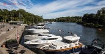Onde ficar em Estocolmo: lindos barquinhos na orla de Estocolmo durante o verão, com o mar azul, vegetação verde e o céu com algumas nuvens brancas