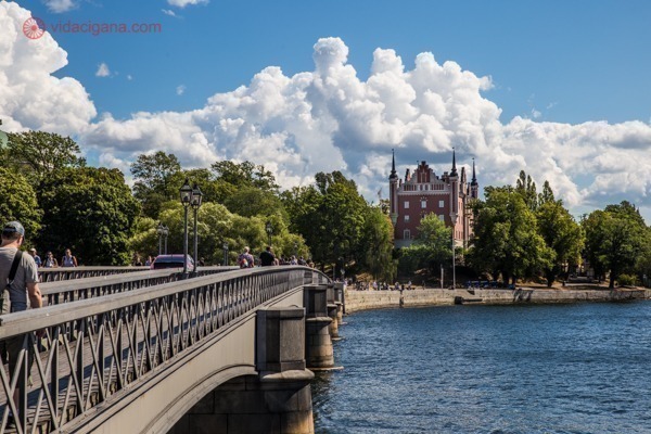 Onde ficar em Estocolmo: A Ponte das Coroas, com vista para uma ilhota com um prédio marrom ao fundo, cheio de árvores. O céu está azul com nuvens brancas