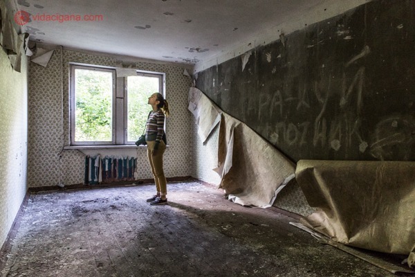 Como visitar Chernobyl: Uma mulher está parada dentro de um apartamento em Chernobyl, com a parede atrás totalmente descascada.