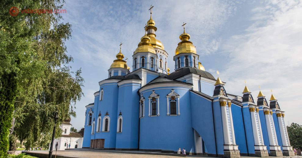 O que fazer em Kiev: A Catedral de São Miguel das Cúpulas Douradas, com suas paredes azuis, cúpulas douradas, num pátio com árvores e céu azul