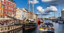 Passeio de barco em copenhague: O porto de Nyhavn, com suas casinhas coloridas na esquerda, um barco ancorado ao lado das casinhas e um barco cheio de turistas saindo do canal