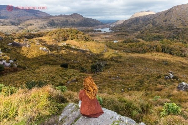 Roteiro Irlanda: Uma mulher, de cabelos ruivos, se senta na borda de uma pedra em Ladies View, no Parque Nacional Killarney
