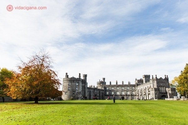 Roteiro Irlanda: O lindo Castelo de Kilkenny, super bem conservado, com uma árvore em tons de outono em sua frente, num enorme gramado verde