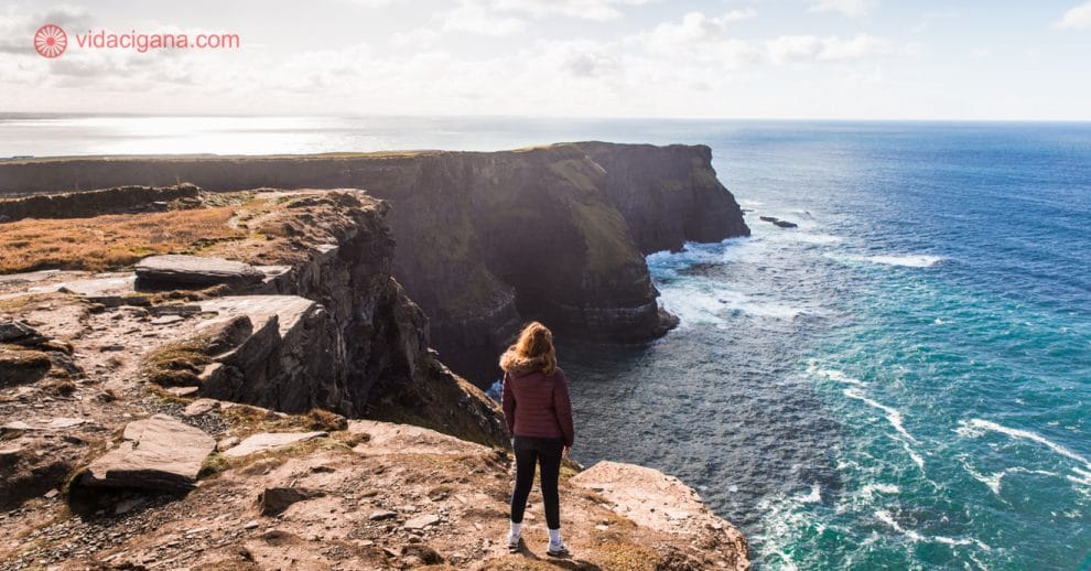 Aluguel de carro pela Irlanda: uma mulher ruiva na beira de um precipício na Irlanda, olhando o mar