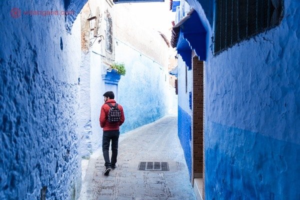 Chefchaouen, a cidade azul do Marrocos: Um homem de casaco laranja caminhando pelas ruelas da medina de Chefchaouen, onde as paredes são todas azuis