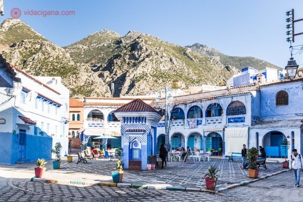 Chefchaouen, a cidade azul do Marrocos: A praça Bab el-Sor, com a fonte no centro e os prédios azuis em volta, e as montanhas Rife ao fundo.