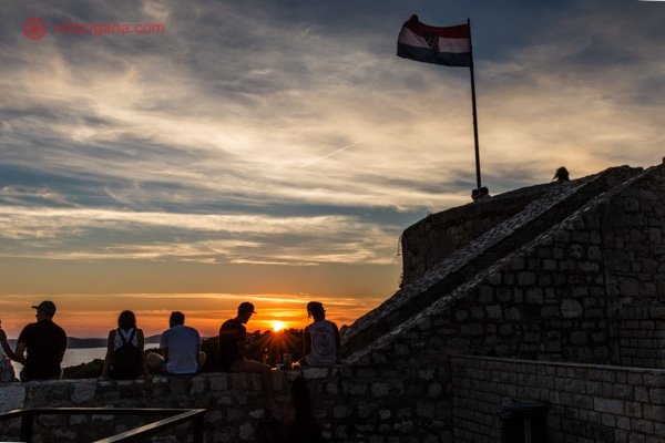 O pôr do sol do alto da Fortaleza Espanhola, com várias pessoas sentadas em sua mureta vendo o céu dourado