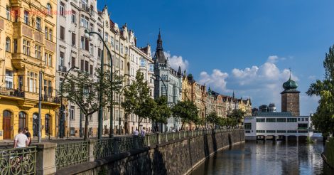 Seguro viagem europa: a cidade de Praga na beira do rio com vários prédios coloridos e árvores na beira do rio.