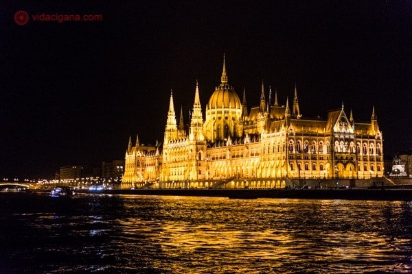 o parlamento de Budapeste visto a noite completamente iluminado de luzes amarelas, na beira do rio danúbio