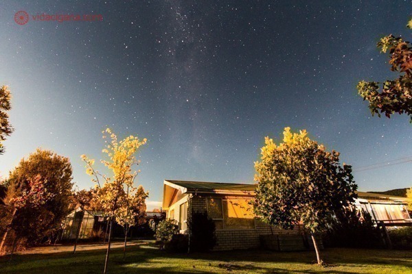 A Via Láctea subindo por trás de uma casa com árvores no entorno