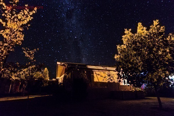 Como fotografar a Via Láctea: A Via Láctea subindo por trás de uma casa iluminada pelos postes a noite