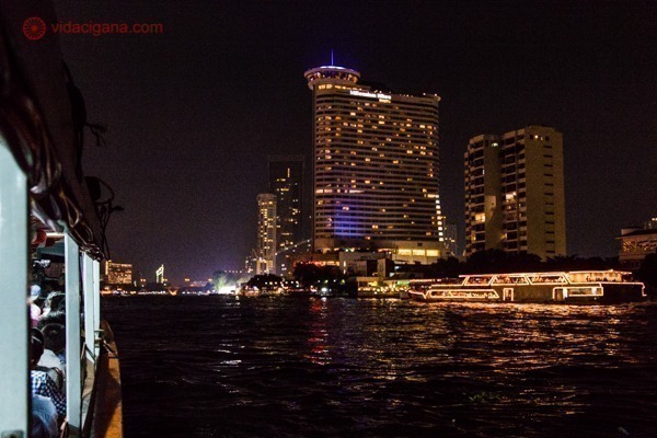 Vista do rio Chao Phraya durante a noite com os barcos iluminados e grandes hotéis ao fundo