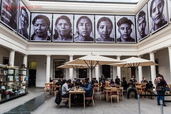 O que fazer em Santiago: o átrio principal do Museu de Arte Pré-Colombiana, com várias mesas com pessoas tomando café, uma galeria de fotos de pessoas descendentes de indígenas no topo do prédio