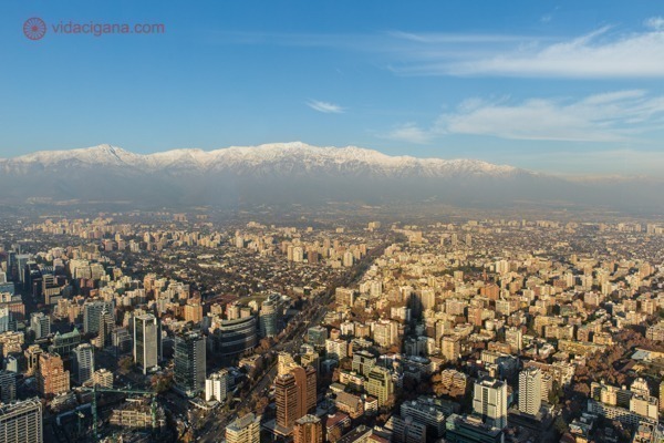 Santiago vista do topo do Sky Costanera, com a Cordilheira dos Andes ao fundo, a sombra do edifício sobre os prédios abaixo