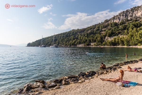 Onde ficar em Split: Uma das praias afastadas de Split, com poucas pessoas tomando sol na beira do mar, cercado por uma colina cheia de vegetação