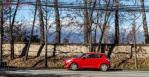 Aluguel de carro no Chile: um carro vermelho numa estrada no Chile com árvores secas atrás e a cordilheira dos andes no fundo com neve