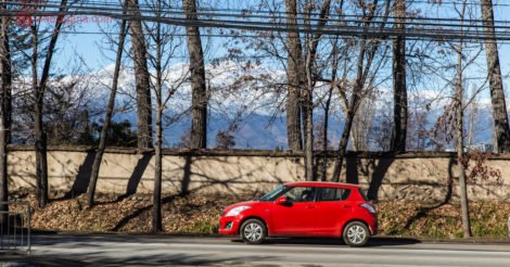 Aluguel de carro no Chile: um carro vermelho numa estrada no Chile com árvores secas atrás e a cordilheira dos andes no fundo com neve