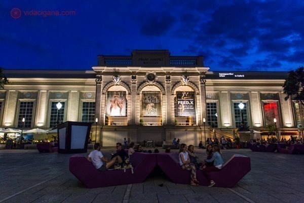 o museumsquartier, em Viena, de noite, cheio de pessoas sentadas na frente dos museus