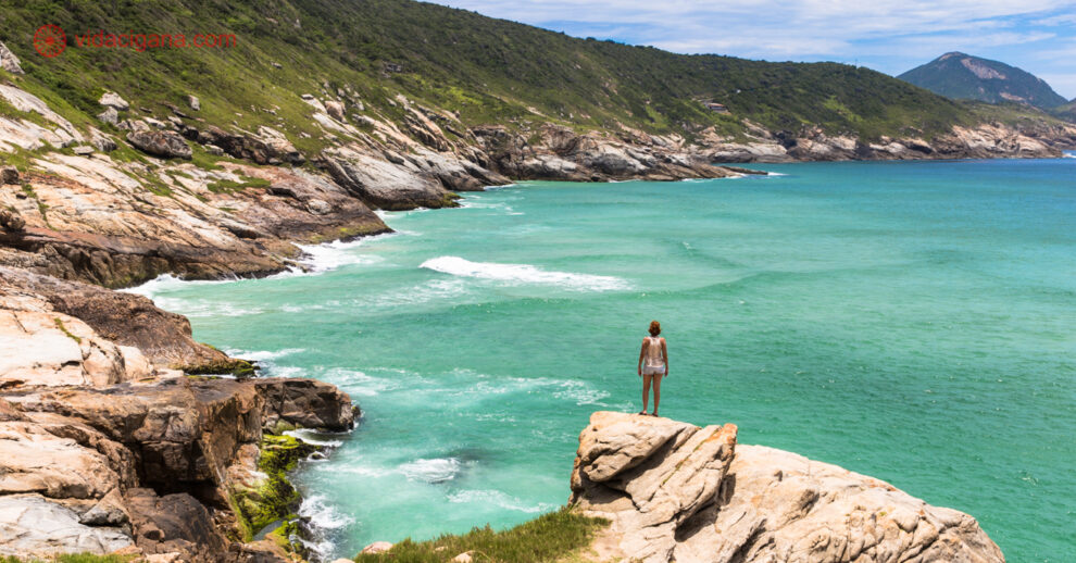 O que fazer em Arraial do Cabo: uma mulher no topo de uma pedra de frente ao mar verde