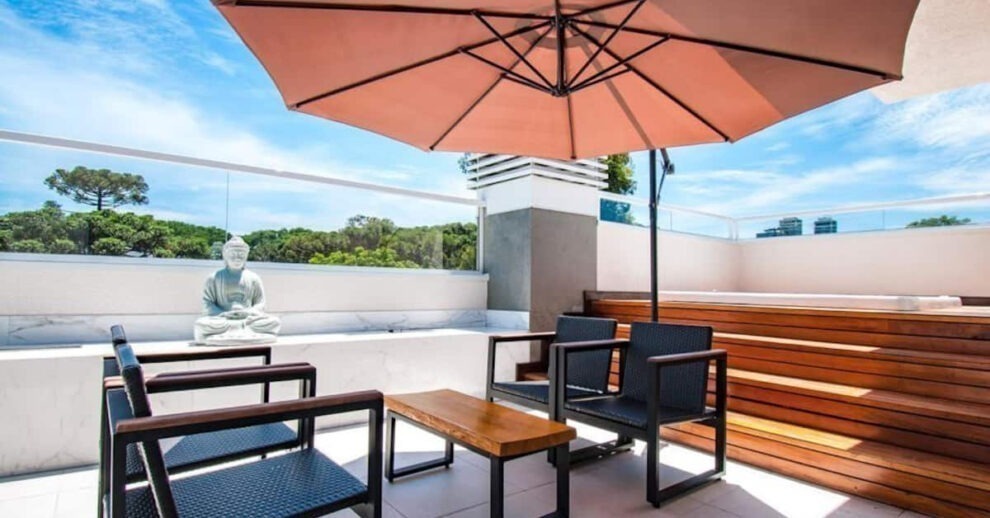 Airbnb em Curitiba: um terraço com cadeiras de sol e um guarda sol e estátua de Buda
