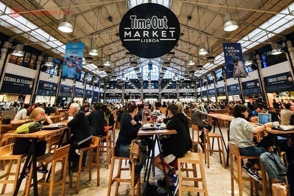 O Mercado da Ribeira, conhecido como Time Out Market, visto do chão, com mesas em todos os lados e restaurantes no entorno. Foto tirada antes da pandemia. O Mercado da Ribeira se encontra no Cais do Sodré, na cidade de Lisboa.