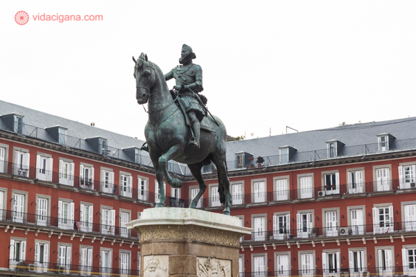 A estátua equestre do rei no meio da Plaza Mayor, com prédios vermelhos ao fundo