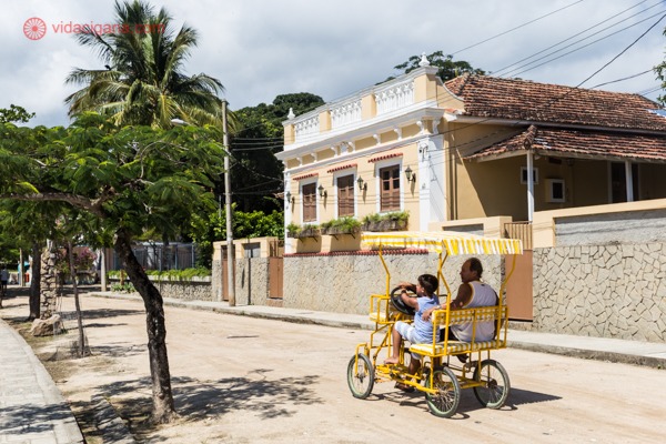 Um homem e um menino dentro de uma bicicleta para 2 pessoas numa rua em Paquetá