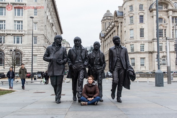 Uma mulher sentada na frente das estátuas dos beatles