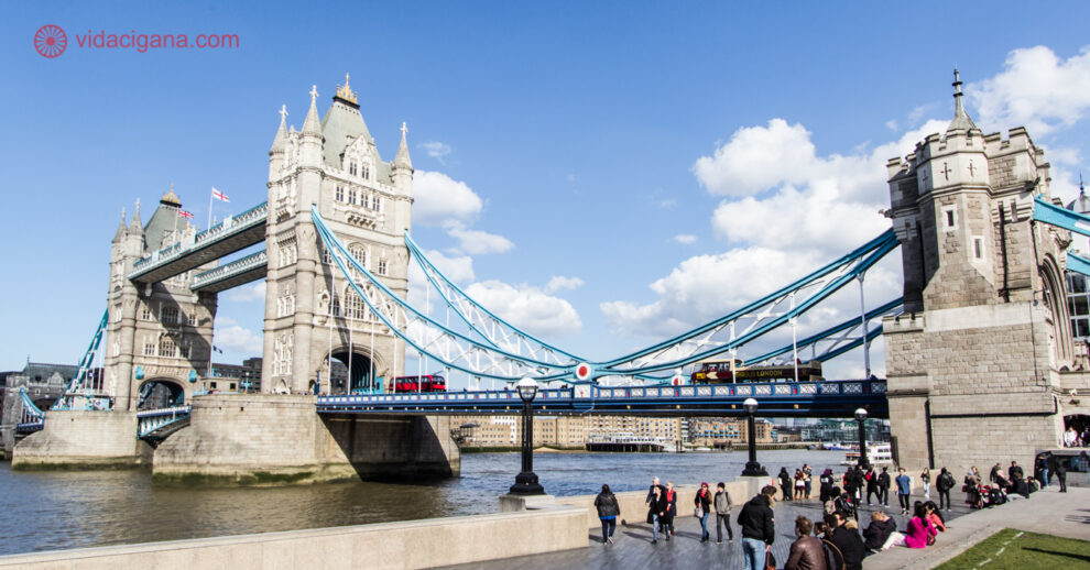 Onde ficar em Londres: A Tower Bridge num dia de sol, com várias pessoas sentadas na beira do Rio Tâmisa.