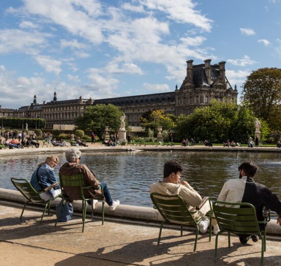 Onde ficar em Paris: O Jardim de Tuilerias, com pessoas sentadas a beira de uma fone, com o Louvre ao fundo